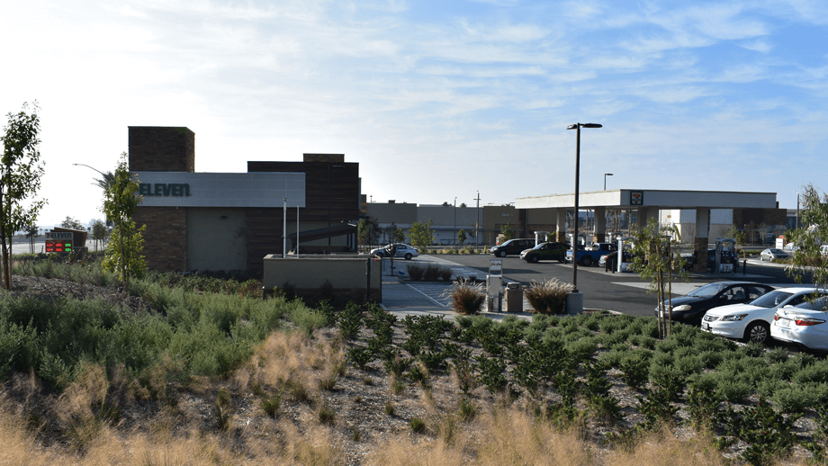 Outdoor image of 7-11 next to a gas station with greenery in the foreground.