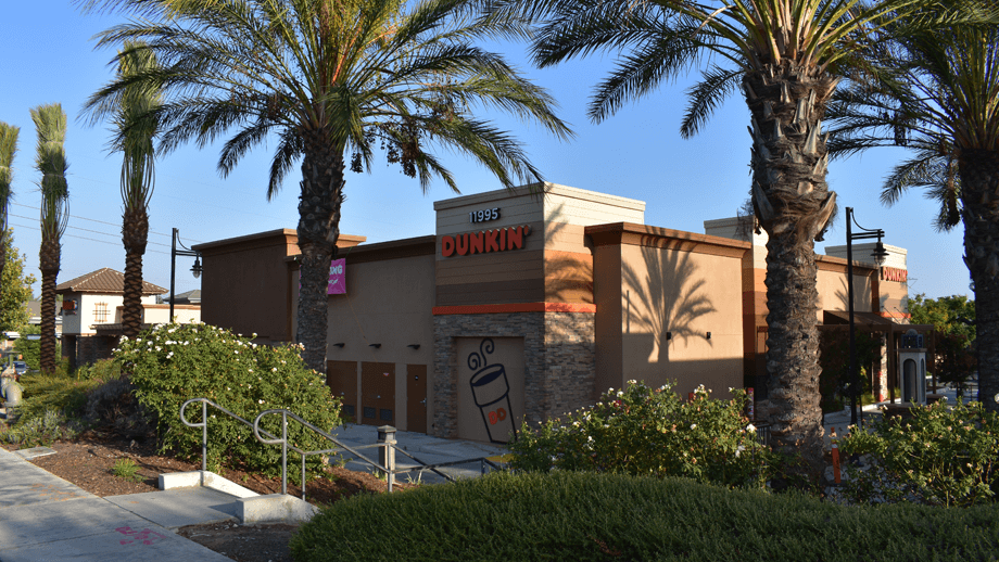 Outdoor image of the back of Dunkin Donuts with greenery and palm trees in the foreground.