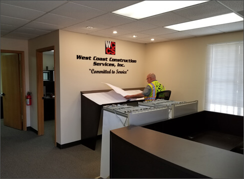 Indoor image of West Coast Construction offices showing technician working on a large desk.